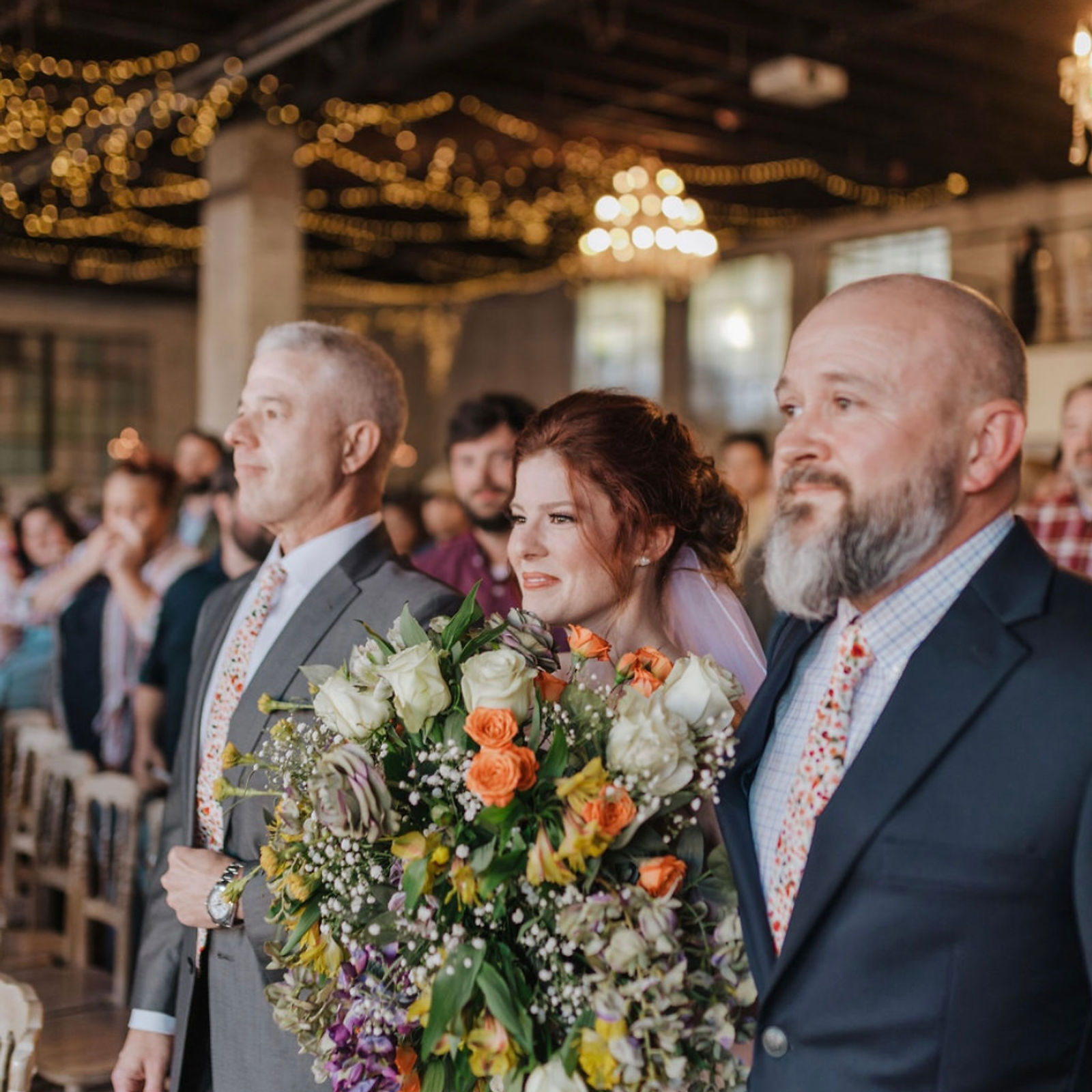 A candid moment of the bride walking down the aisle, flanked by her father and stepfather.