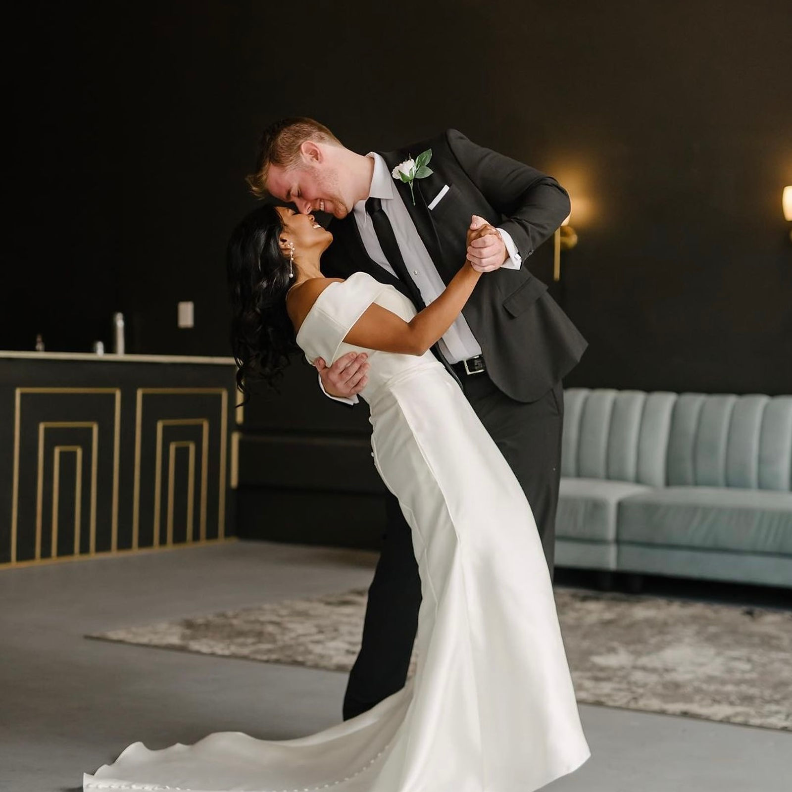 A couple's first dance in the black-walled Art Deco lounge, gold geometric molding on the bar front behind them.