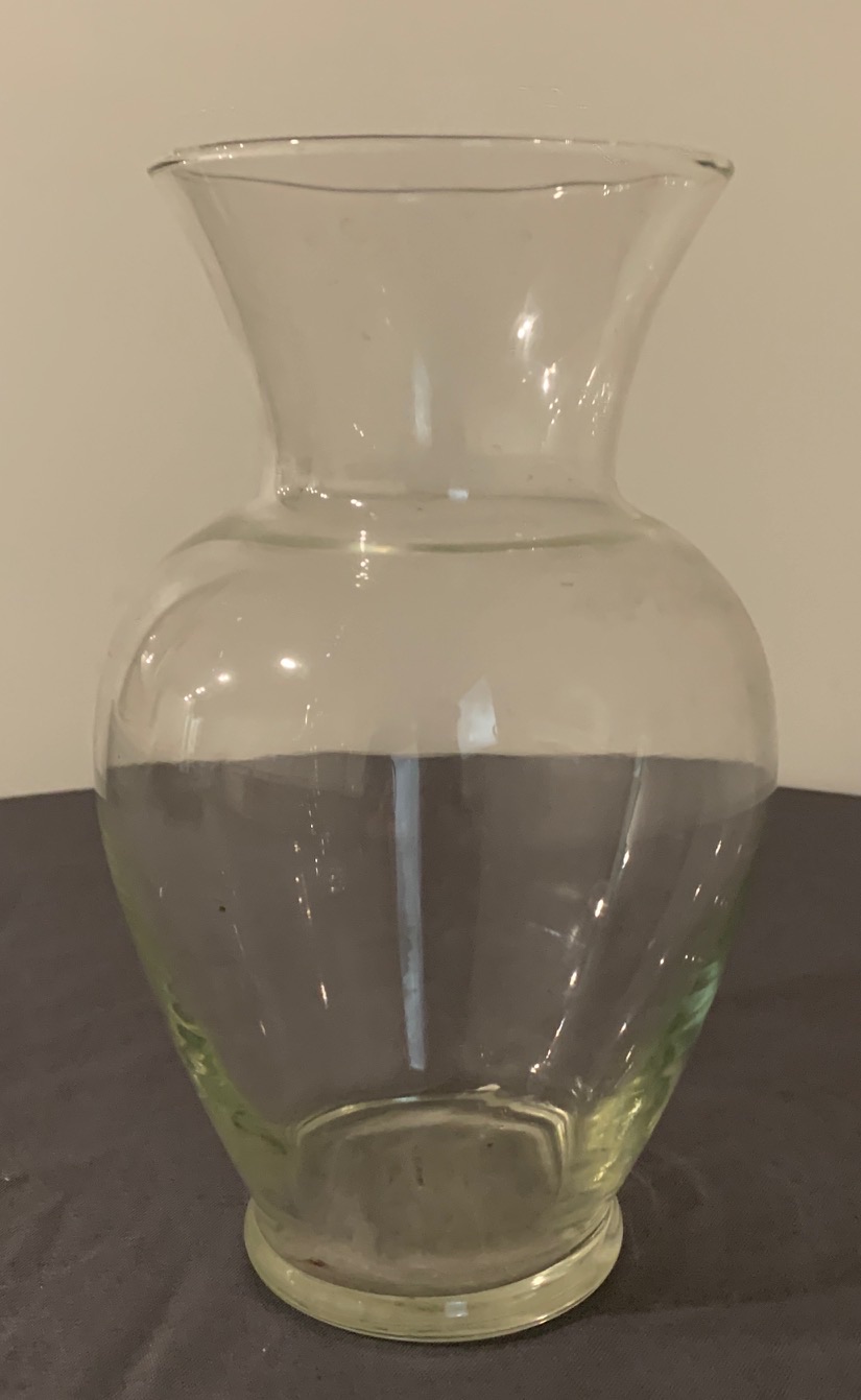 A clear glass urn vase with a rounded body and a flared rim, on a dark table.