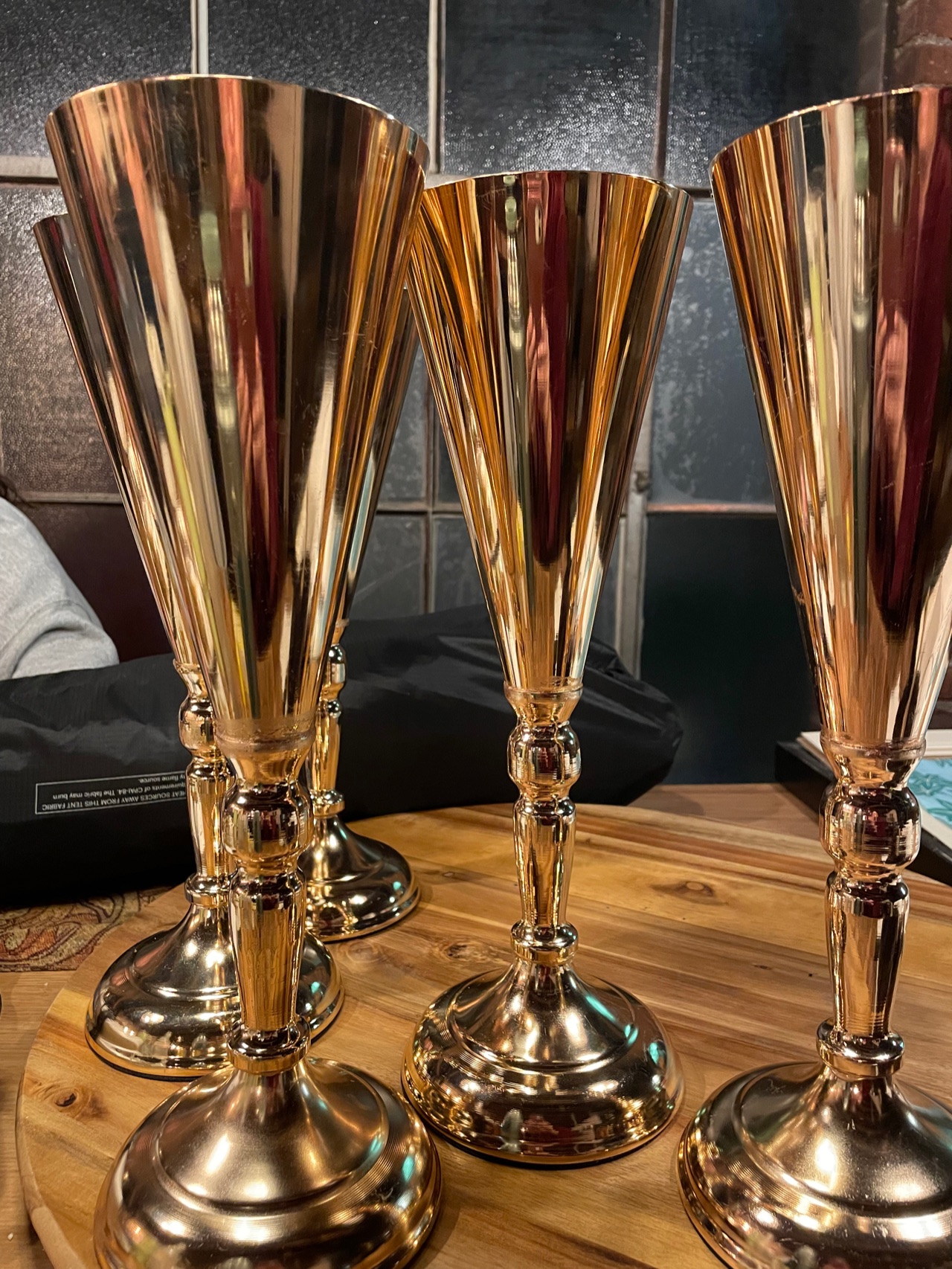 Three tall gold trumpet vases on turned bases, stood together on a wooden table.