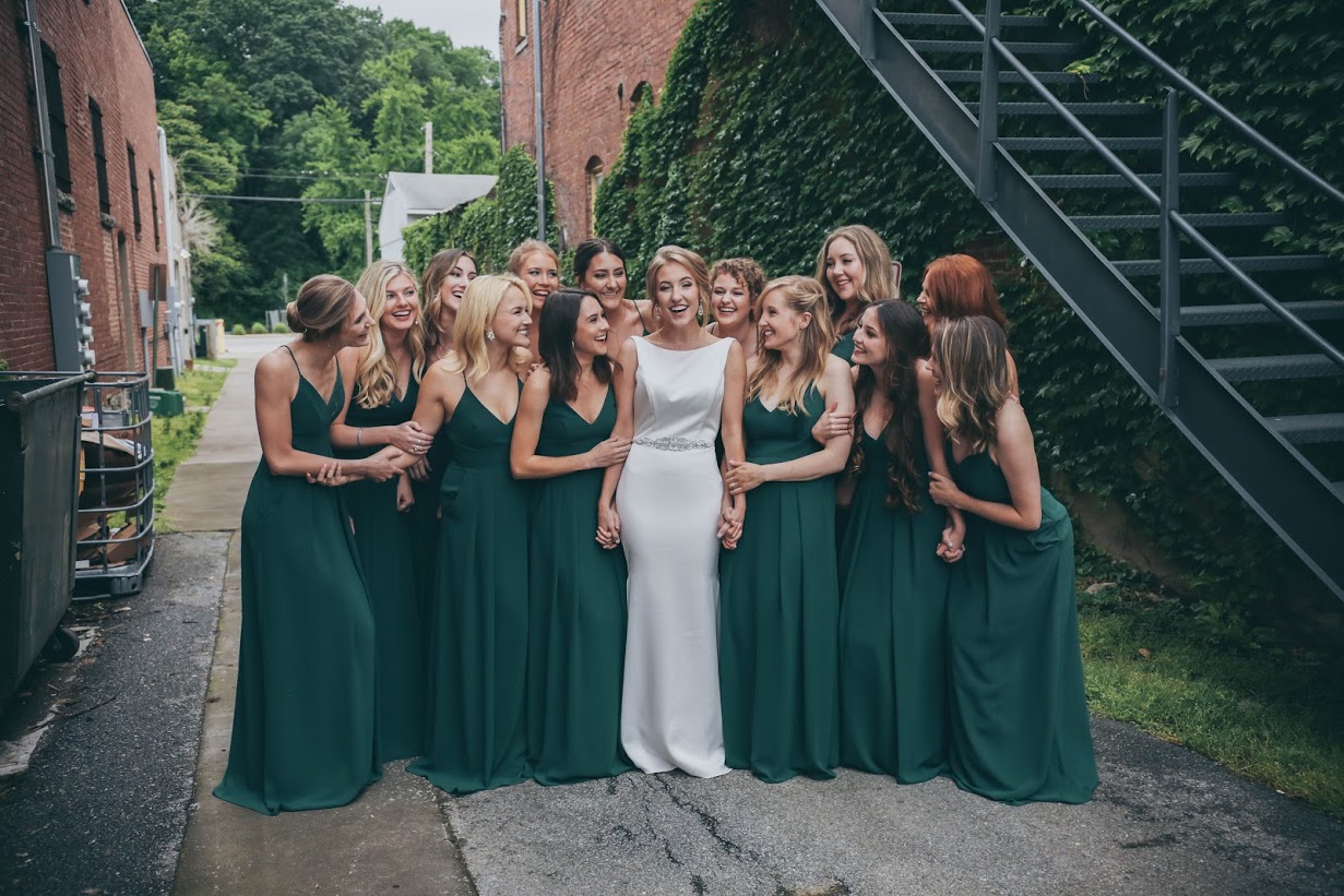The bride and her bridesmaids in emerald gowns, gathered along the ivy-walled alley.