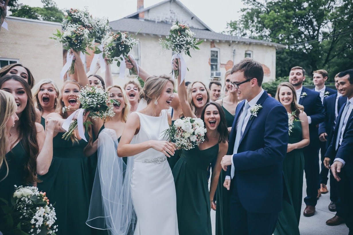 The wedding party cheering with bouquets raised on a downtown street.