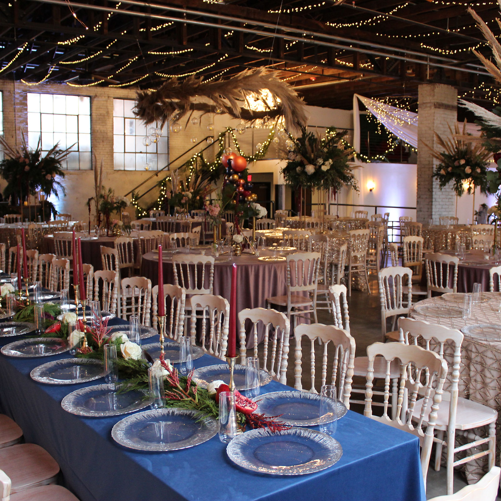 The main ballroom set for an evening reception — long tables, candlelight, pampas grass against the brick.